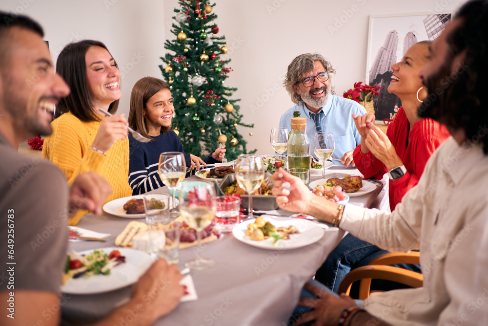 Funny family gathering celebrating Christmas vacations together at festive table. People laughing and eating together at home on Thanksgiving Day. Three Caucasian generations enjoying domestic life. 