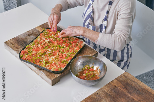 Crop aged woman adding vegetables to pizza