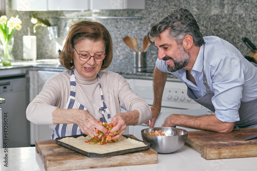 Son and mother cooking pie in kitchen