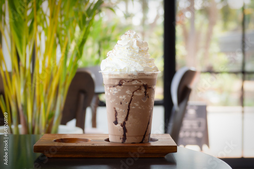 Mocha frappuccino in plastic cup with whipping cream on top. Coffee blended with chocolate. Closeup shot in cafe.