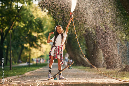 Cooling with the fresh water that goes from the pump. Happy little girl with skateboard outdoors
