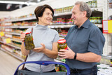 Elderly married couple choosing canned cucumbers together in the grocery section of supermarket