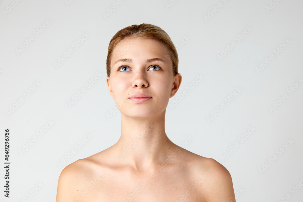 Portrait of attractive girl with smooth, well-kept beautiful skin looking upwards isolated over grey studio background Portrait of attractive girl with smooth, well-kept beautiful skin looking upwards isolated over grey studio background