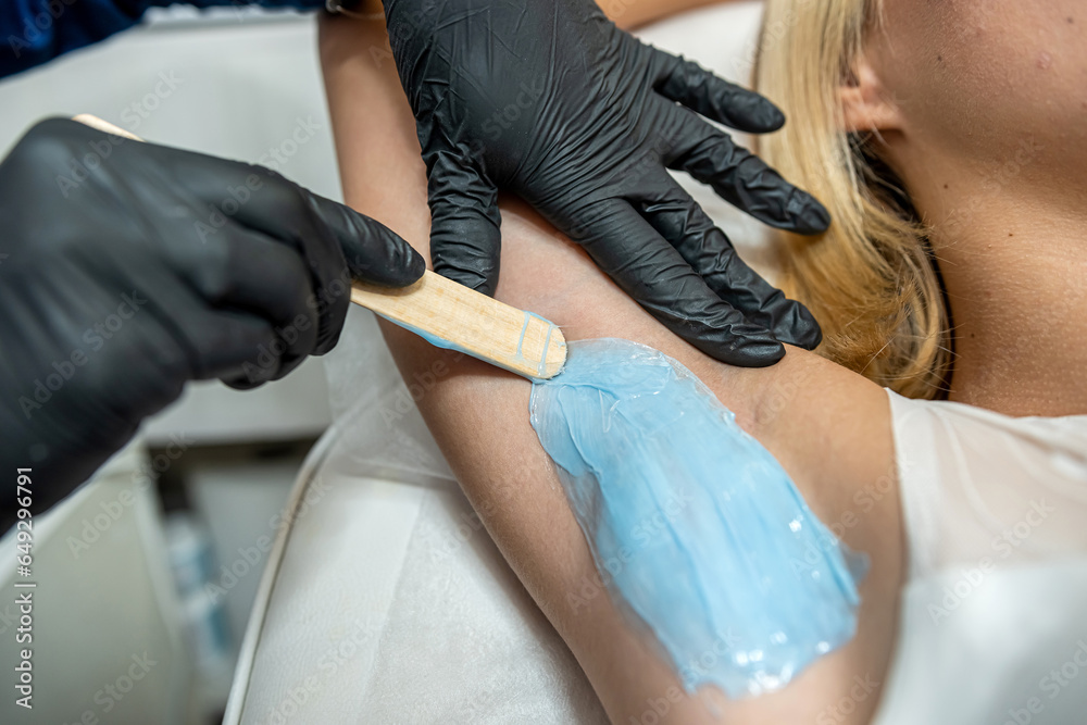 Beautician doing cosmetology procedure is removing hair in armpits with hot wax
