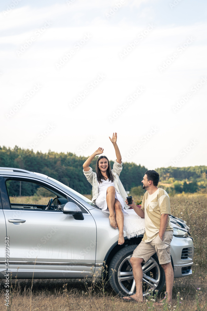 Happy couple enjoy a summer weekend with a car outside the city in a field.
