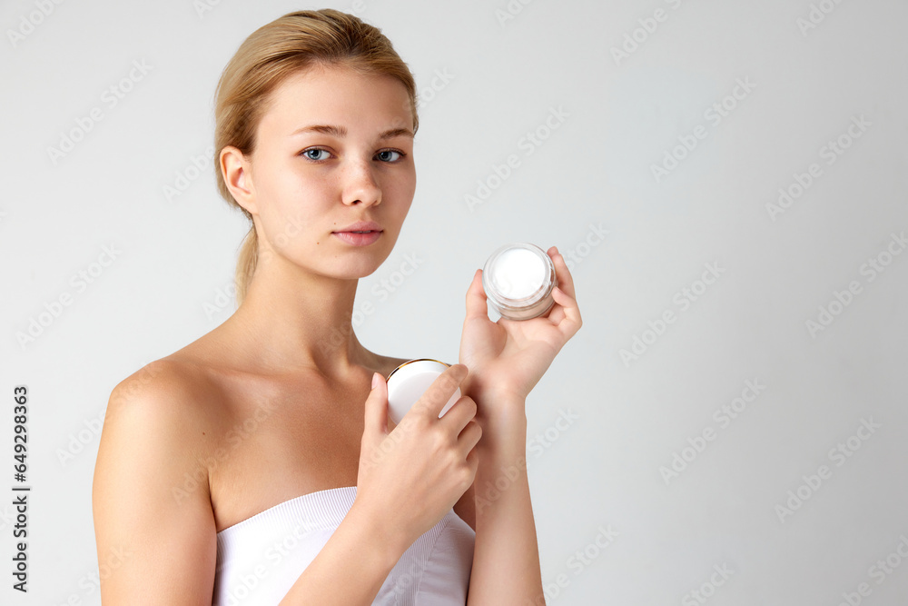 Portrait of attractive young girl taking care after skin with face cream isolated over grey studio background Portrait of attractive young girl taking care after skin with face cream isolated over grey studio background