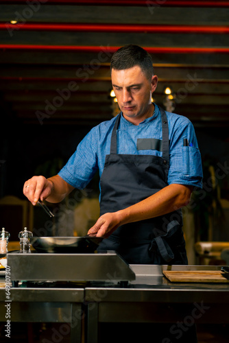 A close-up of a chef with tongs in his hand frying bacon for a burger in the professional kitchen of an Italian restaurant