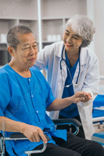 Asian people mature woman doctor giving male elderly patient through indoor physical therapy in a healthcare wheelchair, emphasizing hands-on support and recovery. expert physical therapy