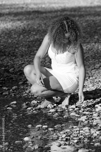 Junge Frau in weissem kleid sammelt Steine am Flussufer