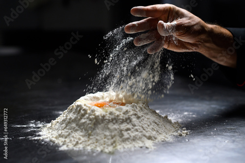 Closeup of chef s hand sprinkling flour  dark background