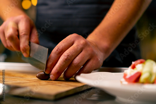 Close-up of a chef cutting olives with a knife while preparing a salad in the kitchen of an Italian restaurant