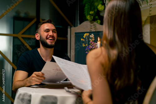 Young couple guy and girl sitting in an Italian restaurant looking at the menu and choosing what to order for dinner while on a date 