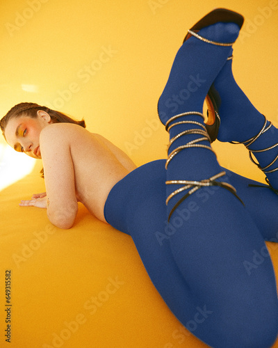 Vibrant fashion shoot featuring a girl in striking blue stockings against a bold yellow backdrop, exuding chic and playful elegance. (ID: 649315582)