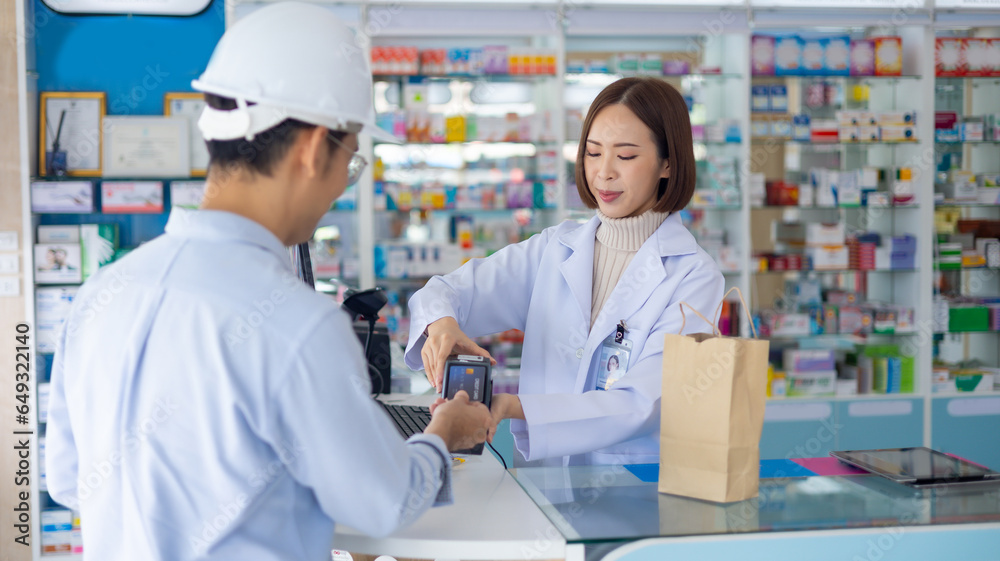 male engineer worker customer buying medication and paying for medicine by credit card. female pharmacist at Drugstore. Professional Pharmacist asian woman at pharma store. Health and wellness center male engineer worker customer buying medication and paying for medicine by credit card. female pharmacist at Drugstore. Professional Pharmacist asian woman at pharma store. Health and wellness center