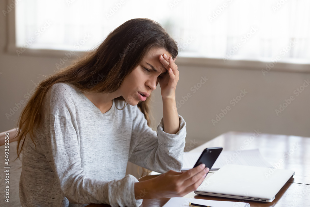 Angry young woman looking at phone screen, reading bad news in email or social network message, unpaid debt or spam, annoyed girl having problem with broken or discharged smartphone Angry young woman looking at phone screen, reading bad news in email or social network message, unpaid debt or spam, annoyed girl having problem with broken or discharged smartphone