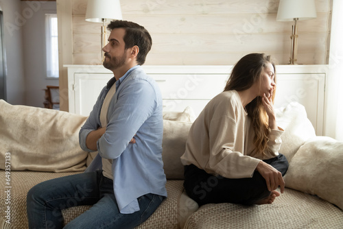 Stubborn offended man and woman ignoring each other after quarrel, unhappy young couple not talking, sitting back to back on couch at home, wife and husband conflict, divorce or break up