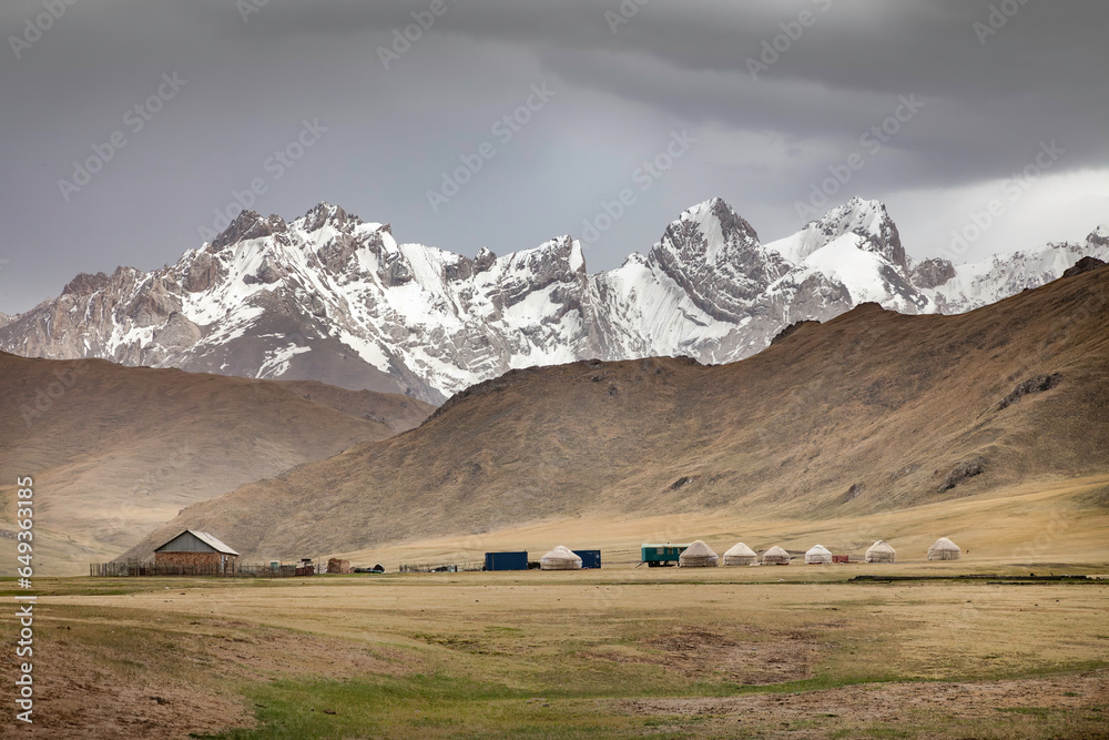 nomadic shepherd camp at the foot of high mountain range of Kyrgyzstan with yurts, a small house and a trailer