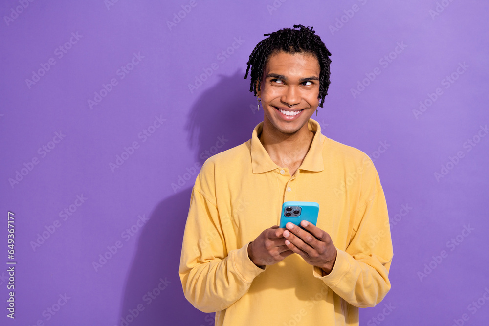 Portrait of funky funny guy with earrings dressed yellow shirt look at empty space smartphone in hands isolated on violet color background Portrait of funky funny guy with earrings dressed yellow shirt look at empty space smartphone in hands isolated on violet color background