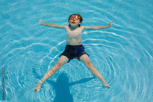 Portrait of happy little kid boy in the pool and having fun on family vacations in a hotel resort. Healthy child playing in water, swimming and splashing.