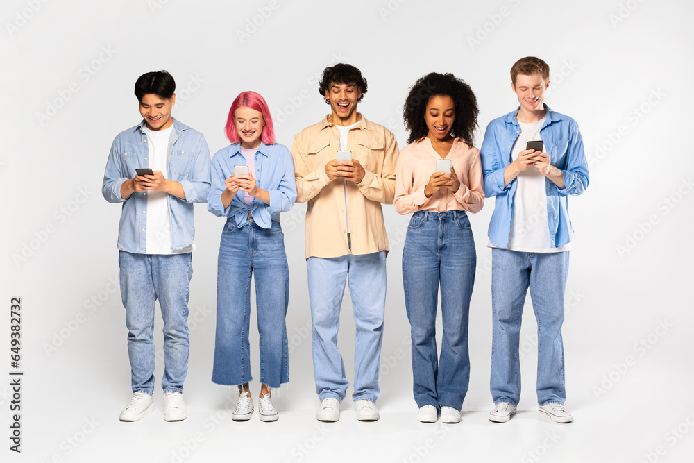 Excited teen multiracial friends company chatting using their cellphones, browsing internet posing over white background