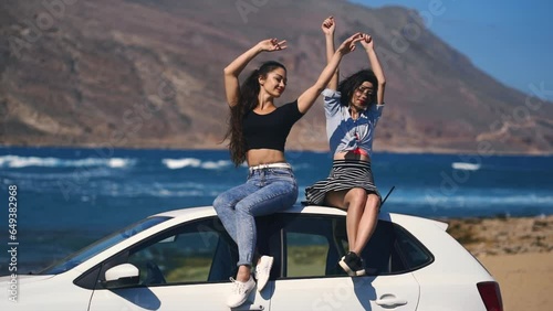 Epic summer road trip, two best friends laughing and watching the sea coastline in Greece on road trip at sunset, travel and adventure lifestyle. Two women girls enjoy holiday vacation lourney photo