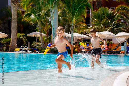 Two happy little kid boys jumping in the pool and having fun on family vacations in a hotel resort. Children playing in water with a water gun. Laughing running siblings brothers and best friends photo