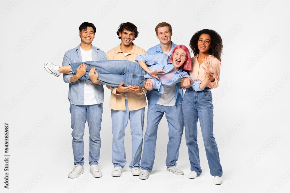 Youth and fun. Group of excited multiracial students holding friend and smiling at camera, white background, full length