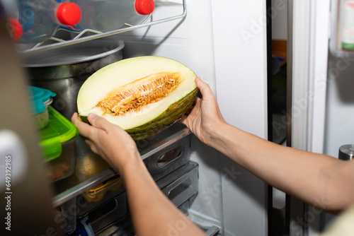 woman's hands saving or putting a started melon from the refrigerator. refrigeration of fruit at home