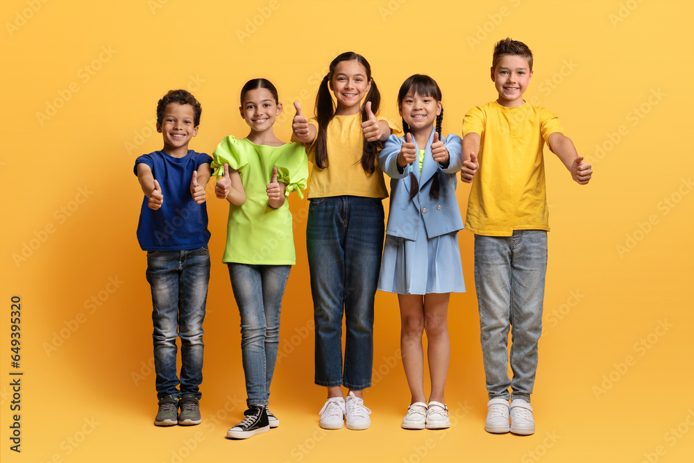 Fototapeta premium Cute school aged kids posing on yellow, showing thumb ups