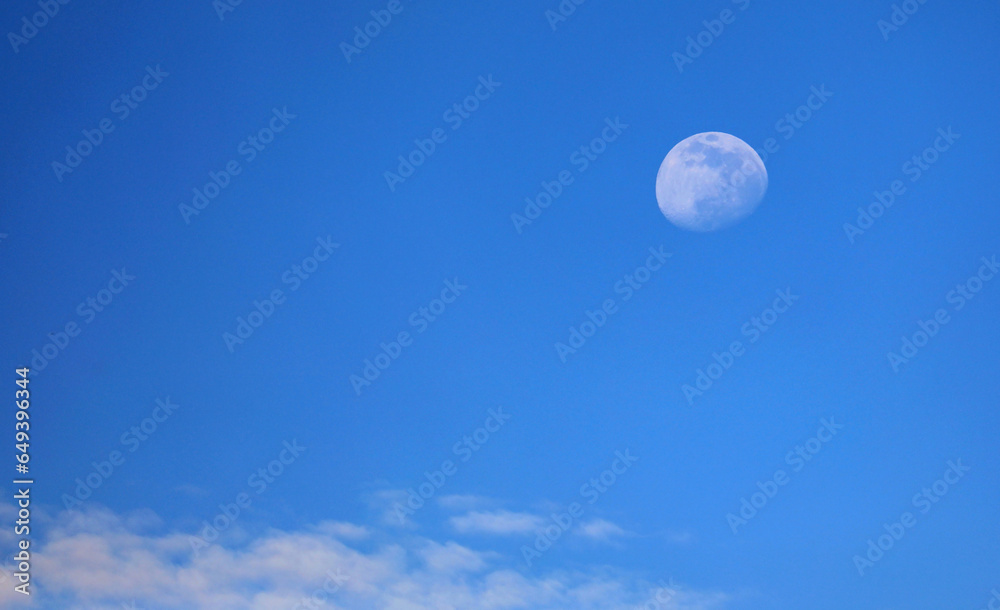 White moon almost full and blue sky with some clouds at daytime White moon almost full and blue sky with some clouds at daytime