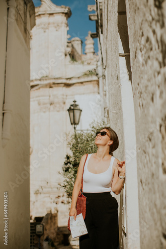 Female tourist with paper city map on narrow streets of Ostuni, Italy