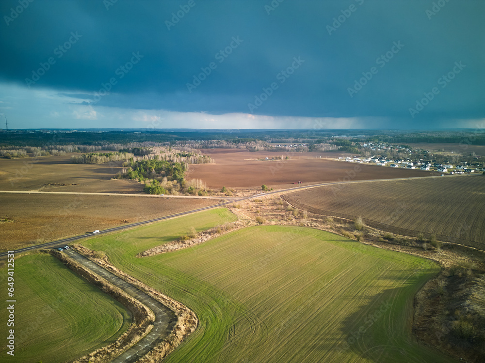 A dark thundercloud is moving over a rural field. A cloud with a clearly visible rain line. Aerial view over an agricultural field during rain. The drone is flying in a field in the rain.