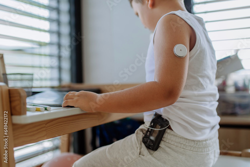 The diabetic boy doing homework, while wearing a continuous glucose monitoring sensor on his arm. photo