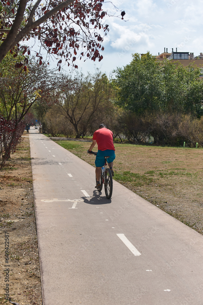 Obraz premium Unrecognizable cyclist on the bike and electric scooter lane in the middle of a public park.