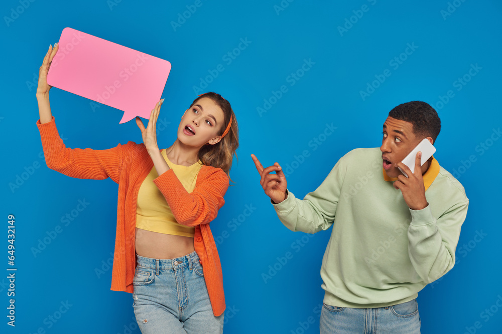 amazed african american man in glasses pointing at woman with speech buttle on blue background amazed african american man in glasses pointing at woman with speech buttle on blue background