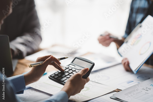 Young colleagues discuss business and analytical price charts using calculators and laptops to calculate financial, tax, accounting, statistics and analytical research ideas.