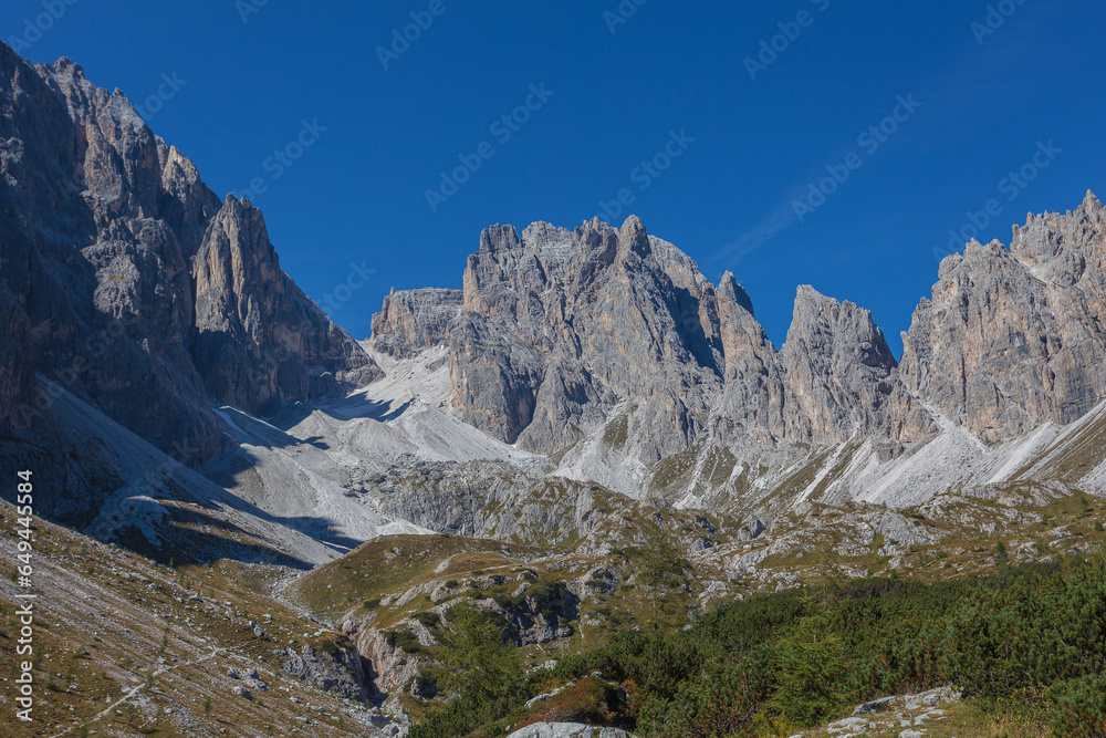 Rocky ridge of Croda Rossa di Sesto Mountain in Comelico region with green meadows and blue sky, Dolomites, Italy