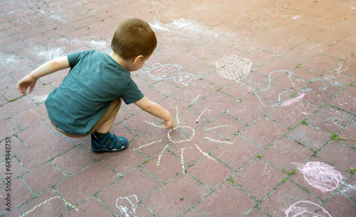 Little toddler boy two or three years old draws sun with crayons in the park on tiles. Playtime for children. Children's games. Selective focus