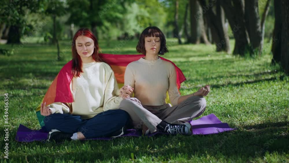 Lesbian couple practicing yoga in the park take a yoga poses while sitting down on the grass they have meditation time Lesbian couple practicing yoga in the park take a yoga poses while sitting down on the grass they have meditation time