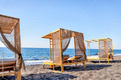 Fototapeta Naklejka Na Ścianę i Meble -  Fira, Greece - July 20, 2023: Palapas and beach chairs on the island of Santorini in Greece
