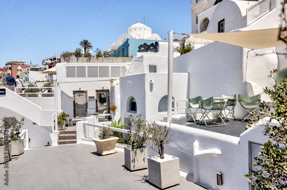 Naklejka premium Fira, Greece - July 20, 2023: Cliffside buildings and walkways in the town of Fira on the island of Santorini in Greece