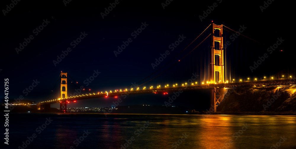 Golden Gate Bridge at night with a reflection on the bay.
