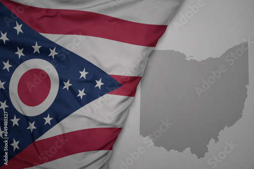 big waving national colorful flag and map of ohio state on the gray background.