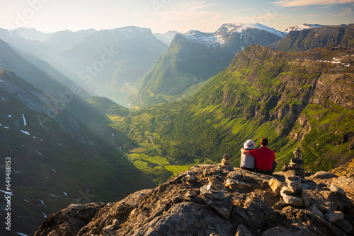  A couple takes in the view from Europe's highest fjord viewpoint by road, overlooking the town of Geiranger from the Skywalk, 1500 meters above sea level.