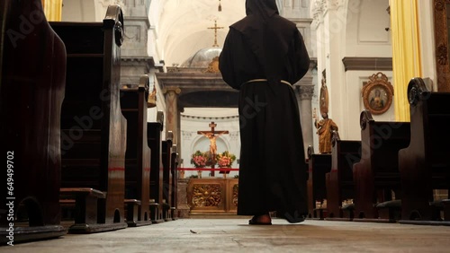 Fraile franciscano monje sacerdote caminando en oración meditando rezando hincado ante el altar con Cristo al fondo en templo iglesia parroquia en la casa de Dios photo