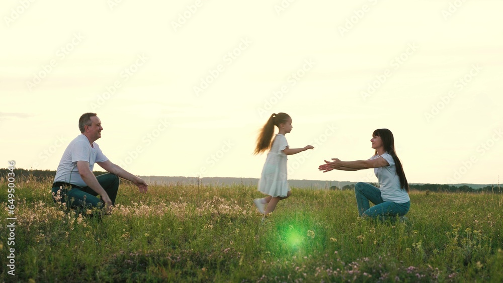 Cute little girl runs from loving mother to father paying in summer field