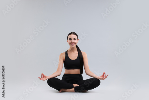 Beautiful young woman practicing yoga on grey background. Lotus pose