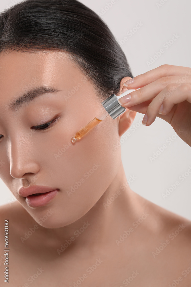 Beautiful young woman applying cosmetic serum onto her face on white background, closeup Beautiful young woman applying cosmetic serum onto her face on white background, closeup