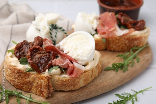 Delicious sandwiches with burrata cheese, ham and sun-dried tomatoes on white table, closeup