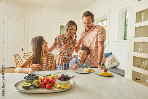 Smiling family with two children (8-9, 12-13) eating fresh fruit in kitchen photo